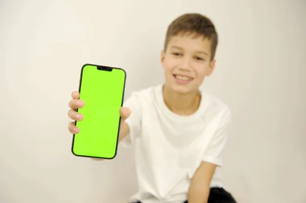 boy 10 years old holding mobile phone with green screen white background white t-shirt blurred space for text ad joy travel toys networks internet online layout for your app or website design project