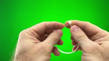 On a green background, a chromakey man fastens a nylon tie with his own hands. He pulls the long end through the hole and secures it nylon tie