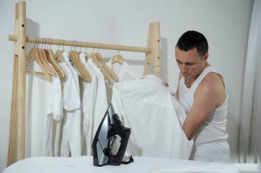 man twisting his sleeve Man doing laundry at home Tired handsome man doing household work, being ready to iron clothing, needs ironing, posing isolated over white Turning shirt sleeves hairy arms