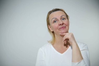  adult woman makes faces as if worm is peeking out of bullseye raised eyebrows open eyes and lips with finger she holds chin Smurf big eyes place for text contented happy plays