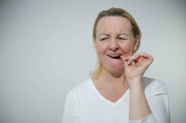 woman has toothache she picks tooth with finger and takes out food stuck real person homemade nails with manicure no makeup no hairstyle unpainted hair roots have grown out looks to side white clothes