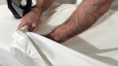 Housework and housework men ironing a shirt on an ironing board at home. Hot steam from iron. Close-up of a mans body in a white T-shirt ironing clothes on an ironing board Shirt hanger background
