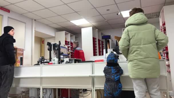 全体的に小さな子供を持つ女性は 棚の上に背景に小包を過ぎて歩く販売人の乗務員を待っている間に小包を配達ノヴァポスタをカウンターに来ましたウクライナVinnitsa 2023 — ストック動画