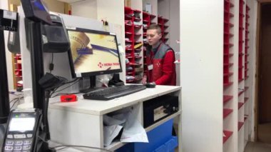 sales assistant at checkout checks documents of client post office equipment new technologies a lot of parcels terminal computers red clothes with new mail sign Ukraine Vinnitsa 2023