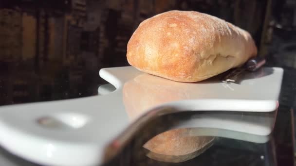 フランスパンの新鮮なローフCiabattaパンは白いPorcelianovaに立っており ボードの横にはおいしいと健康的な食品パン屋のペストリー手作りの食品磁器ボードのテキストコンセプトのためのナイフの場所です — ストック動画