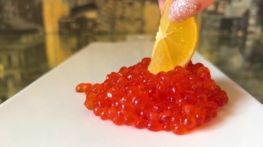  bunch of red caviar lies on white porcelain board female hand shiny manicure inserts piece of lemon into caviar caviar spreads on sides tasty food fish oil benefits need for omega-3 healthy eating
