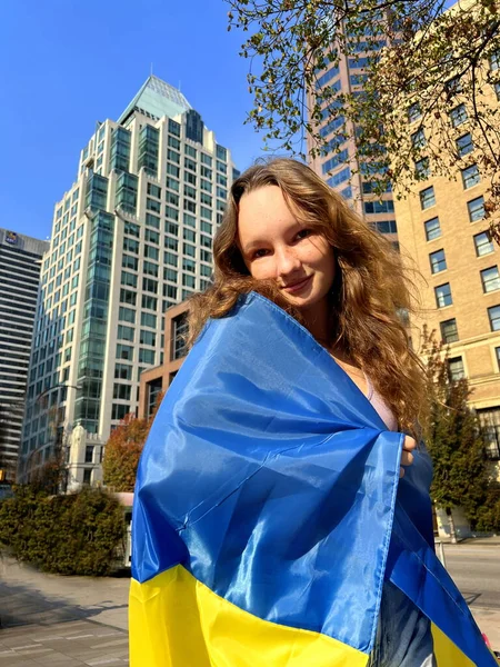 Pray for Ukraine. child with the Ukrainian flag on street. A little girl waving the national flag prays for peace. Happy kid celebrating Independence Day Teenager in downtown Vancouver against war