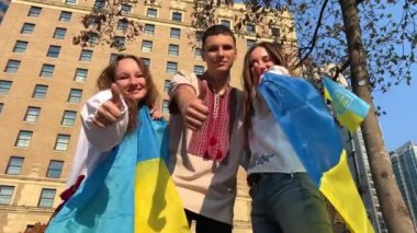 teenagers in embroidered shirts show thumb up independence day victory joy of returning home ukrainian vyshyvanka city center flag of ukraine children joy two girls and one boy children young people