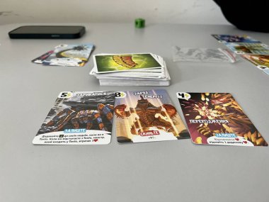 Young guys play board game Richard Garfield owner Tokyo They throw cubes and laying out cards moving chips on a paper playing field on a table Four people sitting at the table and fun spend time