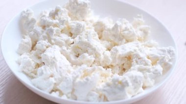 cook breaks raw chicken egg into a cup with homemade crumbly cottage cheese. A close-up view from above Woman adding egg into bowl with cottage cheese for preparing pancakes at kitchen table, closeup