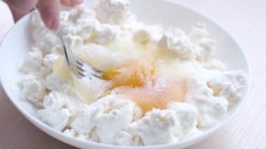 in white plate close-up cottage cheese egg sugar female hands knead egg with fork piercing yolk mixing with cottage cheese stuffing for cheesecake desserts for casseroles force woman kneads stuffing