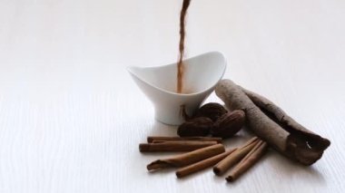 cinnamon and nutmeg cinnamon sticks Aromatic Spices on Wooden Cutting Board with a White Background Cinnamon is poured in a small stream into the White plate, it opens around flying dust