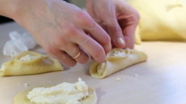 close-up Womans hands with wedding ring are molding dumplings or pies with cottage cheese she is molded from edge of pattern of homemade baking live fresh yeast dough on light table homemade