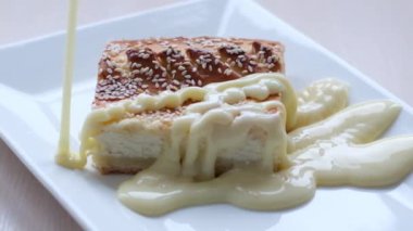 thin stream of condensed milk pours over a delicious curd dessert sweetness is reflected very sweetly on white plate, as if mother-of-pearl