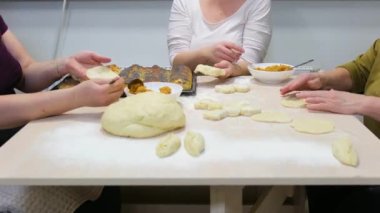 women bake pies at home in kitchen they put carrots cabbage pumpkin in pie and wrap it with dough on table full baking sheet Pies sprinkled with poppy seeds strudel with apple delicious filling