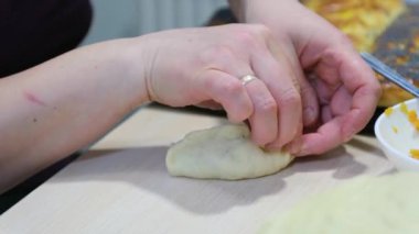 real people hands of adult middle-aged woman with wedding ring are sculpting pies with carrots and pumpkins she is gently pouring one pie In background ready-made baked strudel with poppy seeds
