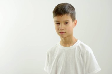 boy of 8-10 years old looks into frame there is place for text white background he is little sad he has narrow oriental eyes beautiful lips neat hairstyle dark hair white t-shirt little reproachfully