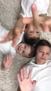 Three brothers lie on heads to each other they wave close camera laugh fool around play make faces older brother 13-15 years old serious middle 8-10 years old smiling small 4-5 years old joyful cute
