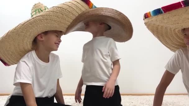 3人の男の子座っています床に家彼らはお互い巨大帽子メキシコの帽子小さなカウボーイセンター5歳の二人のティーネージャー笑顔見ます兄中ティーン乗り物のような馬 — ストック動画