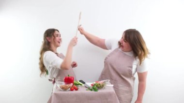 kitchen people fight 2 cheerful women fighting with wooden spoons on white background fun concept of cooking healthy food mom and daughter girlfriends teacher and student aprons kitchen vegetables