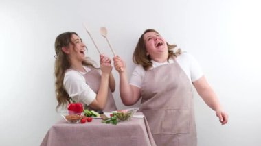 banner 2 cheerful sly smiling chefs with wooden spoons preparing salad identically dressed beautiful women young and middle aged space for text pepper tomatoes vegetable shop restaurant food delivery