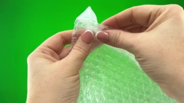 Relieve stress air bubble wrap in hands of woman she presses bubbles that burst soothing nerves on green background chroma key adults Hands of middle-aged woman play and have fun enjoy relaxation
