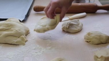 hand of adult woman bakes pies from yeast dough woman with right hand tosses piece of dough in background baking sheet white knife and rolling pin woman lifts dough kneading pizza dumplings