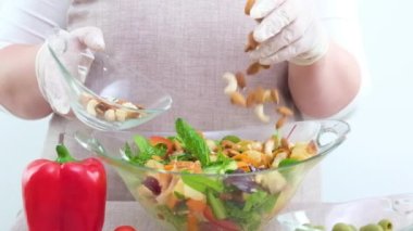 adding nuts to fresh salad vegetarian food almonds hazelnuts cashews many ingredients of green vegetables woman in white gloves and beige aprons close-up only hands delicious diet weight loss healthy