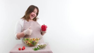 beautiful woman winks showing red bell pepper in hand with other hand showing thumb up class several times pointing at salad vegetarian delicious healthy food for weight loss she winks opening mouth