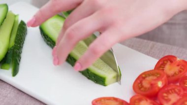 close-up beautiful female young hands cut cucumber with big knife on white porcelain board camera slowly floats shooting tomatoes peppers in glass dish beige background cooking delicious diet food