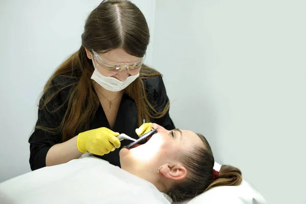 hospital dental clinic doctor examines mouth patient treats the tooth put filling caries doctor in black clothes with mask and glasses patient woman lies with eyes closed place for text