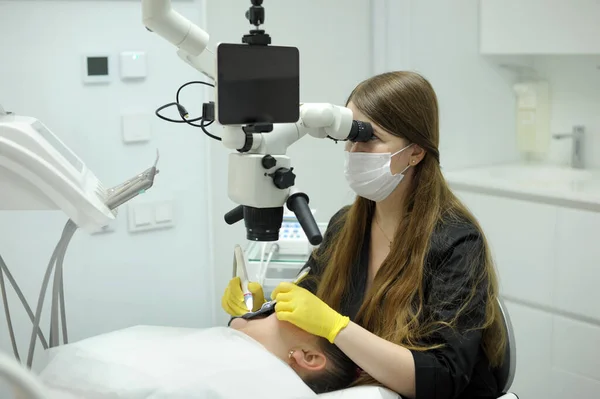 dental clinic latest equipment and technology female doctor treats patients teeth using a microscope with large tablet screen white background space for text advertising yellow gloves black clothes