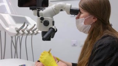 dental clinic latest equipment and technology female doctor treats patients teeth using a microscope with large tablet screen white background space for text advertising yellow gloves black clothes