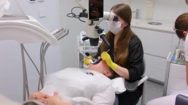 Modern dental equipment Medium shot of female dentist mask gloves using dental microscope to examine patients teeth doctor patient assistant dental treatment prosthetics canals fillings false teeth
