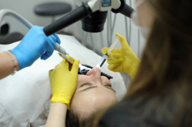 cofferdam clamp for cofferdam The process of dental prosthetics using microscope, female doctor in yellow gloves, patient dentist with patient, using dental curing light