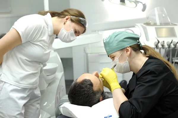 dental clinic doctor removes tooth Patient in yellow gloves in black clothes assistant looks latest technology female doctor and patient man filling caries rotten tooth prosthetics brushing teeth