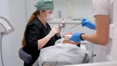 hard tooth extraction, tooth extraction tools Gracie curette, piezo scaler, piezo scaler attachment, piezo scaler wrench, luxator woman doctor dentist removes a man patient tooth heavy easy extraction