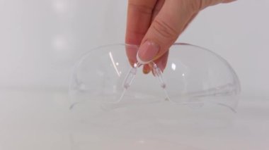 Close up of protective eyeglasses lying on desk in dental office. Dentists glasses on desk. Close-up womans hand takes dentists glasses
