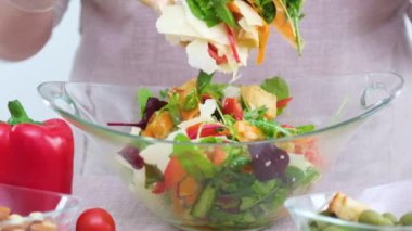 Sebze salatası cam tabağı, kadını karıştırıyor. Büyük kaşık parmesan peyniri, sebze havuçla karıştırılıyor. Ispanak, roka, salatalık, kırmızı çan, vejetaryen.