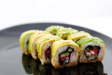 Menü yeşili Japon dürümleri avokado, omlet, susam ve salatalık tabakta yakın plan. Yatay bir şekilde, siyah bir restoranda nefis Japon yemekleri servis ederken.