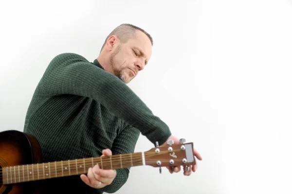 a man tunes a guitar male hands and guitar close-up of a musician playing an acoustic guitar. Music white background advertising green sweater