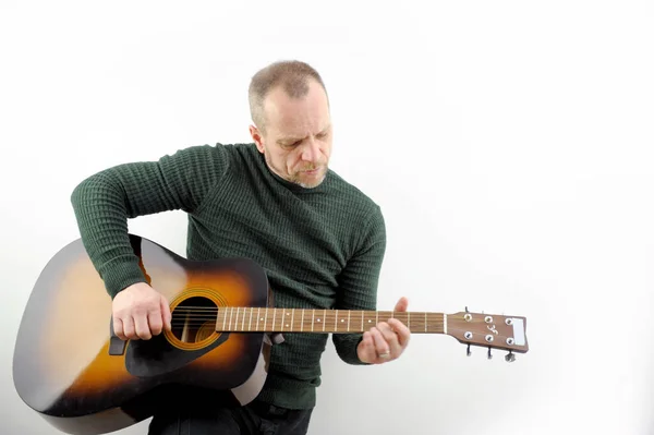 a man tunes a guitar male hands and guitar close-up of a musician playing an acoustic guitar. Music white background advertising green sweater