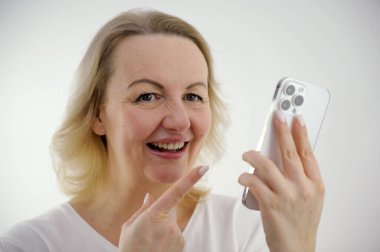 beautiful woman pointing with index finger at white phone she laughs looking at us advertising product pretty win funny joke Is it really so white background Your ad good product online order delivery