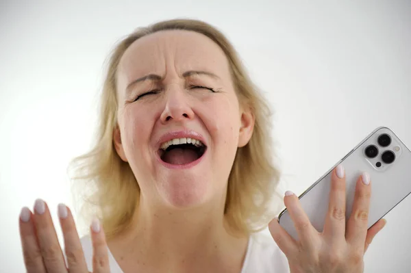 white background close-up woman screaming with her mouth open holding the phone raised hands and spread her fingers to the sides joy dissatisfaction success victory defeat good news bad news