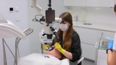 dental clinic latest equipment and technology female doctor treats patients teeth using a microscope with large tablet screen white background space for text advertising yellow gloves black clothes