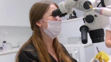 dental clinic latest equipment and technology female doctor treats patients teeth using a microscope with large tablet screen white background space for text advertising yellow gloves black clothes