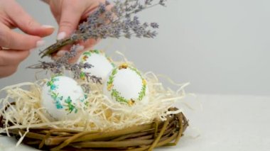 sprigs of lavender female hands lay out near eggs in nest Easter decoration decor place for text of table of contents film about Easter eggs embroidery handmade embroidery with ribbons on eggshells