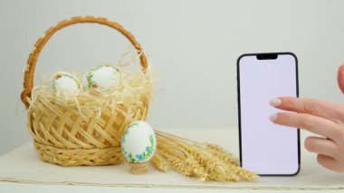 Paskalya bayramı telefonu reklam için boş bir yeri işaret ediyor. Sepet yumurtalarında yumurta desenli işlemeli kurdele yumurta kabuğu buğday çivileri ve hamur sepeti yakın çekim yeri.