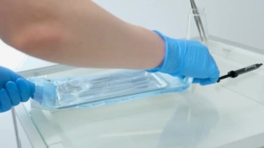 female hands of nurse unpacking sterile instruments after sterilization as well as new cofferdam retractor on glass table dental latest technology for dental treatment black syringe with medicine