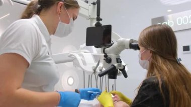 Female patient opening her mouth under the dental microscope and a professional dentist holding tools dentist doctor and nurse treat teeth to a patient using a microscope